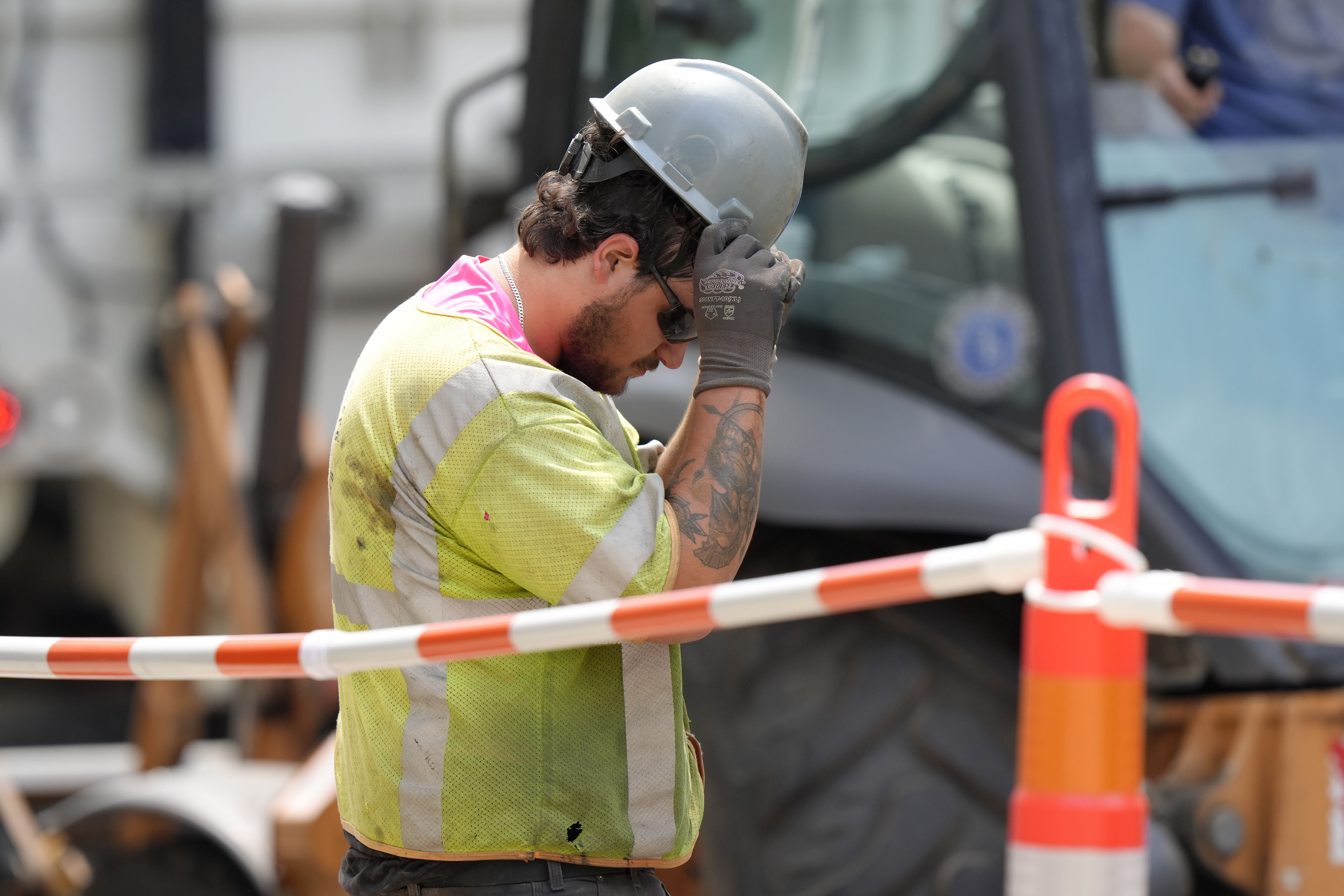 A worker adjusts his helmet while working in temperatures above 90 degrees in Boston. A worker adjusts his helmet while working in temperatures above 90 degrees in Boston.