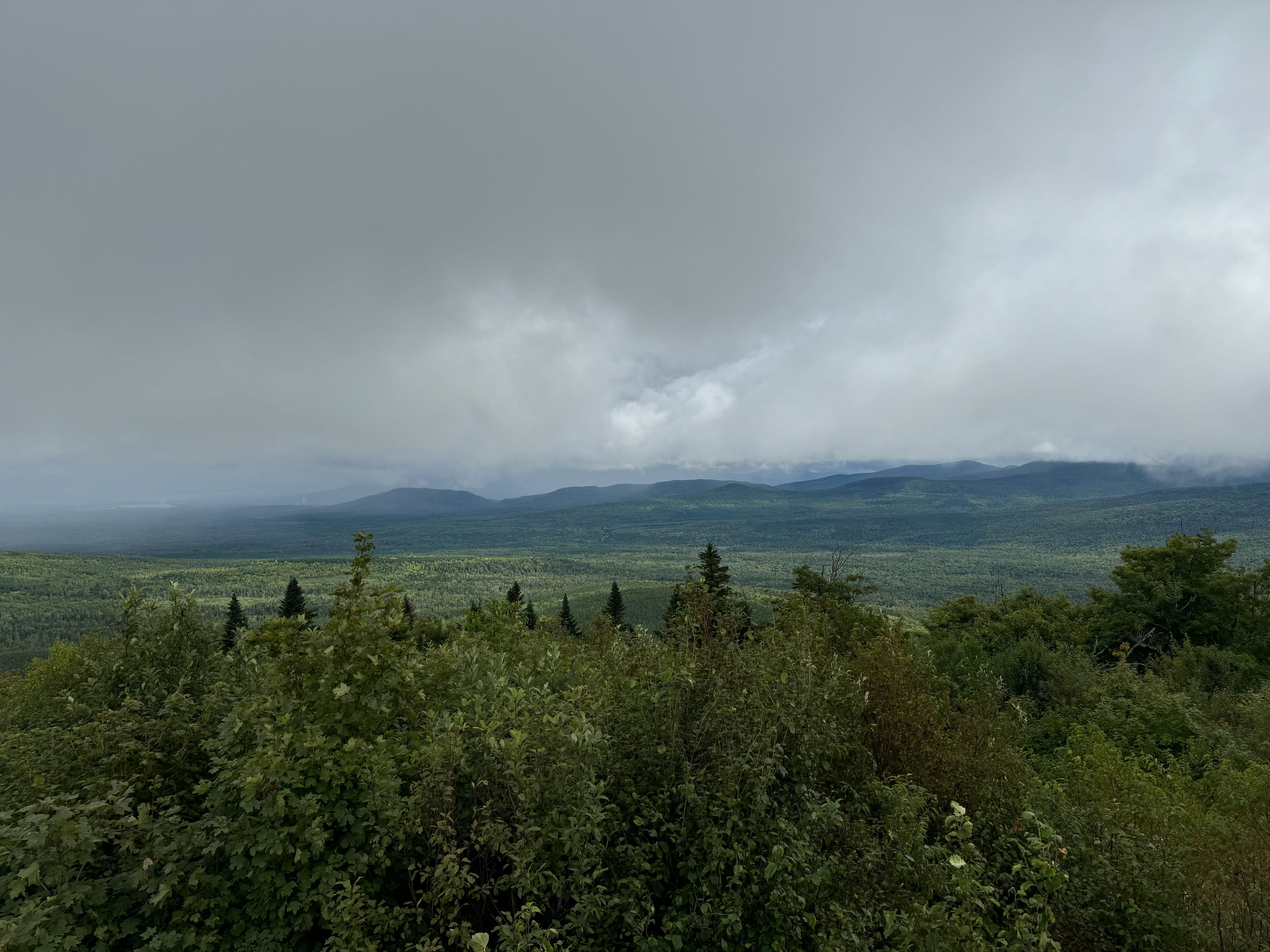 Tree-covered Quill Hill in Maine with gray clouds floating in the sky. Tree-covered Quill Hill in Maine with gray clouds floating in the sky.