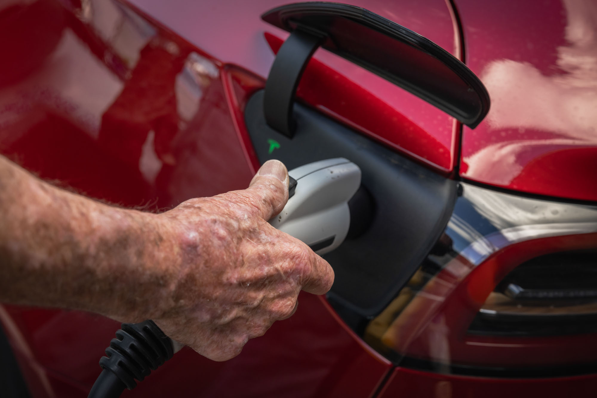 A person attaches a charger to a Tesla. A person attaches a charger to a Tesla.